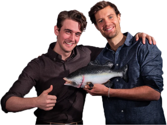 Tom and Emil standing together. Tom is giving a thumbs up and Emily is holding a plastic fish. Tom and Emil both have short brown hair.